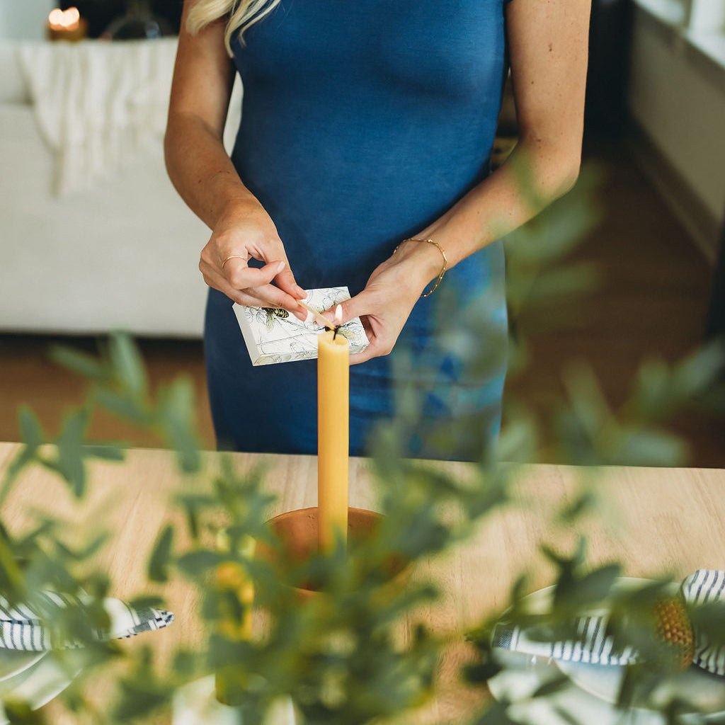 Person lighting a candle with a match, surrounded by greenery indoors.