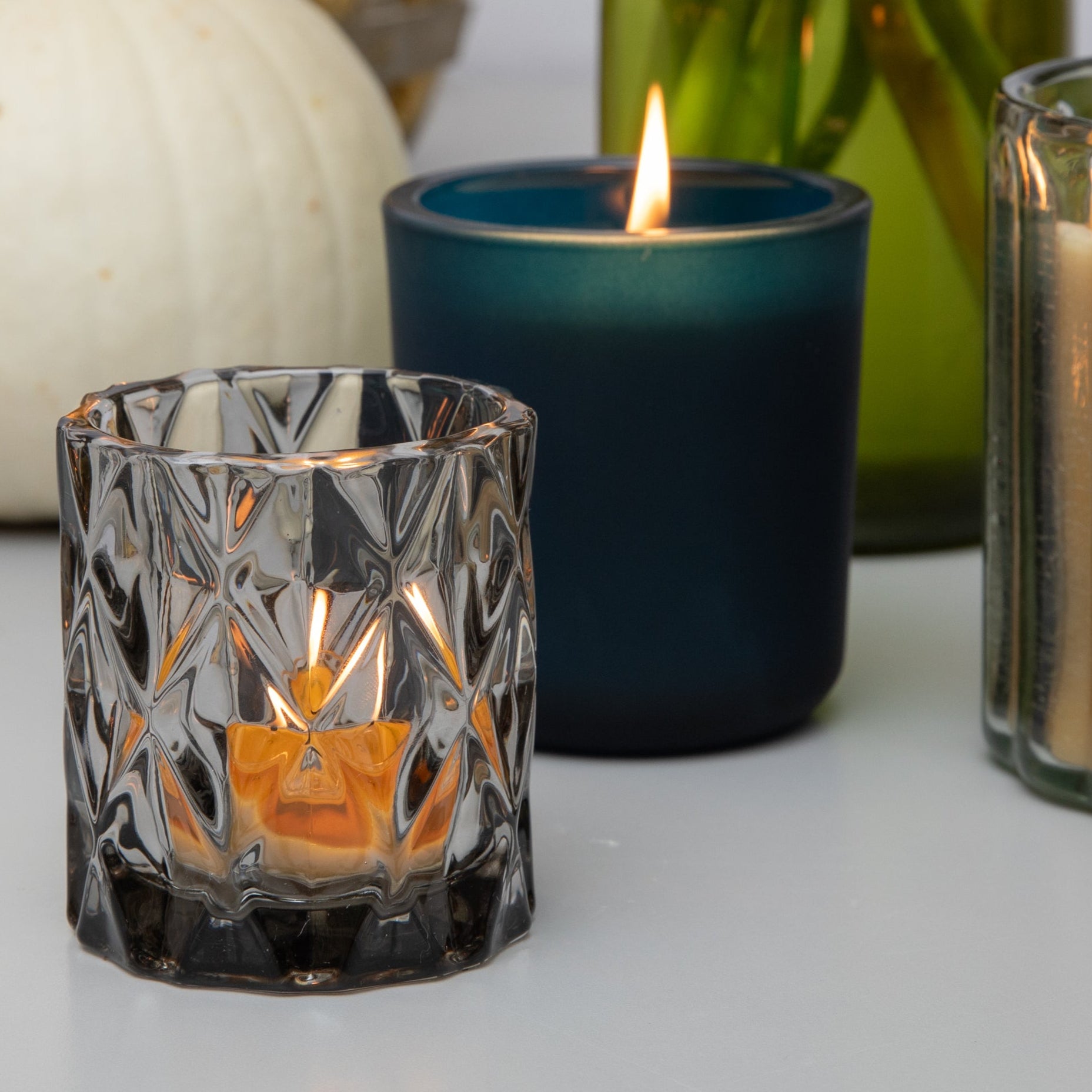 Candles in various holders with a pumpkin and flowers on a table